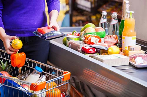 woman at supermarket checkout with shopping trolley and groceries